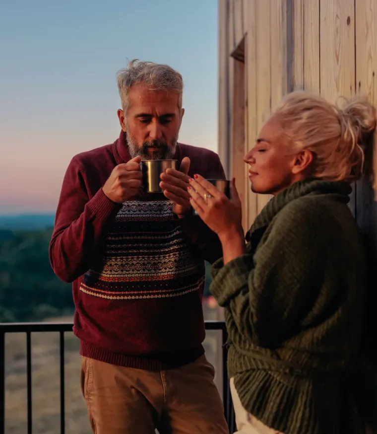 A couple with coffee on a lodge balcony, hills behind them at sunrise