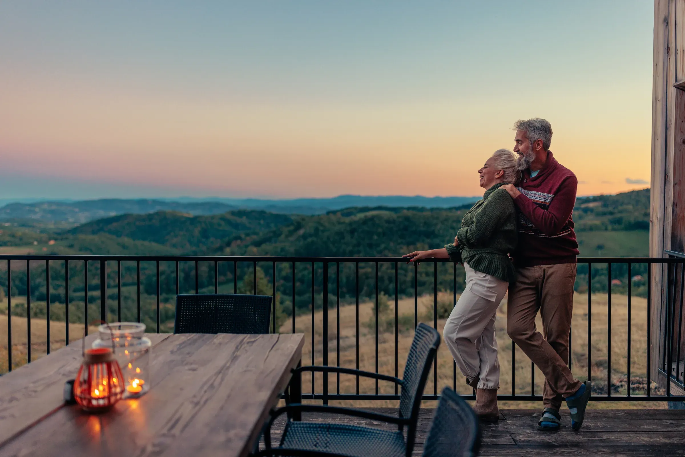 A couple at the rail of their deck at dusk, looking out over the hills