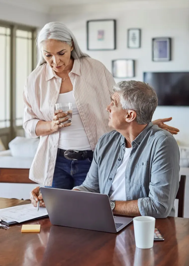 A woman standing over her husband at the table, both reading the same screen