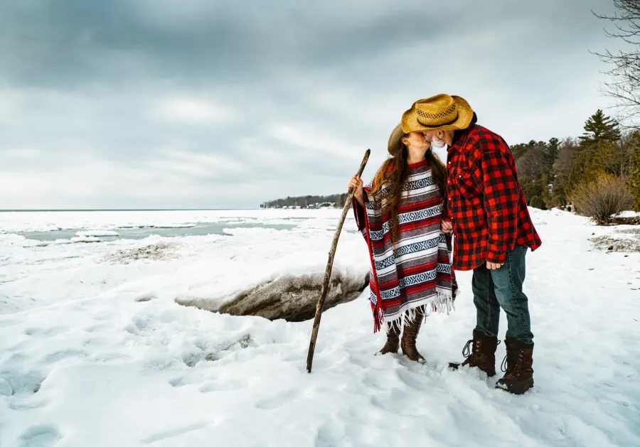 A couple wrapped in a blanket on a lakeshore in winter