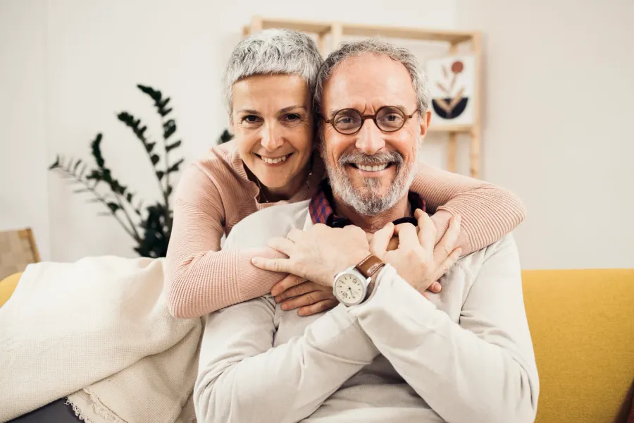 A couple sitting together at home, one arm around the other