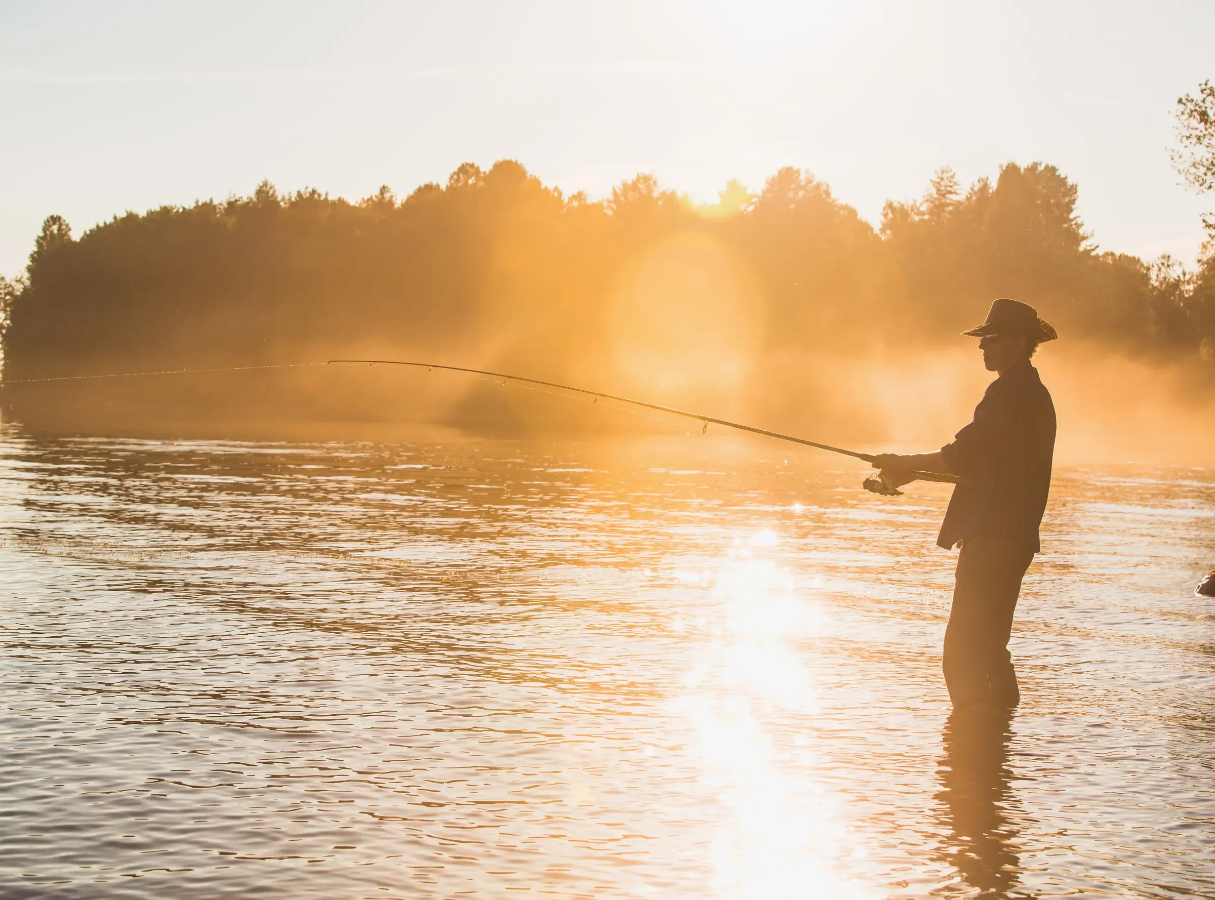 A fly fisherman casting into a river at sunrise