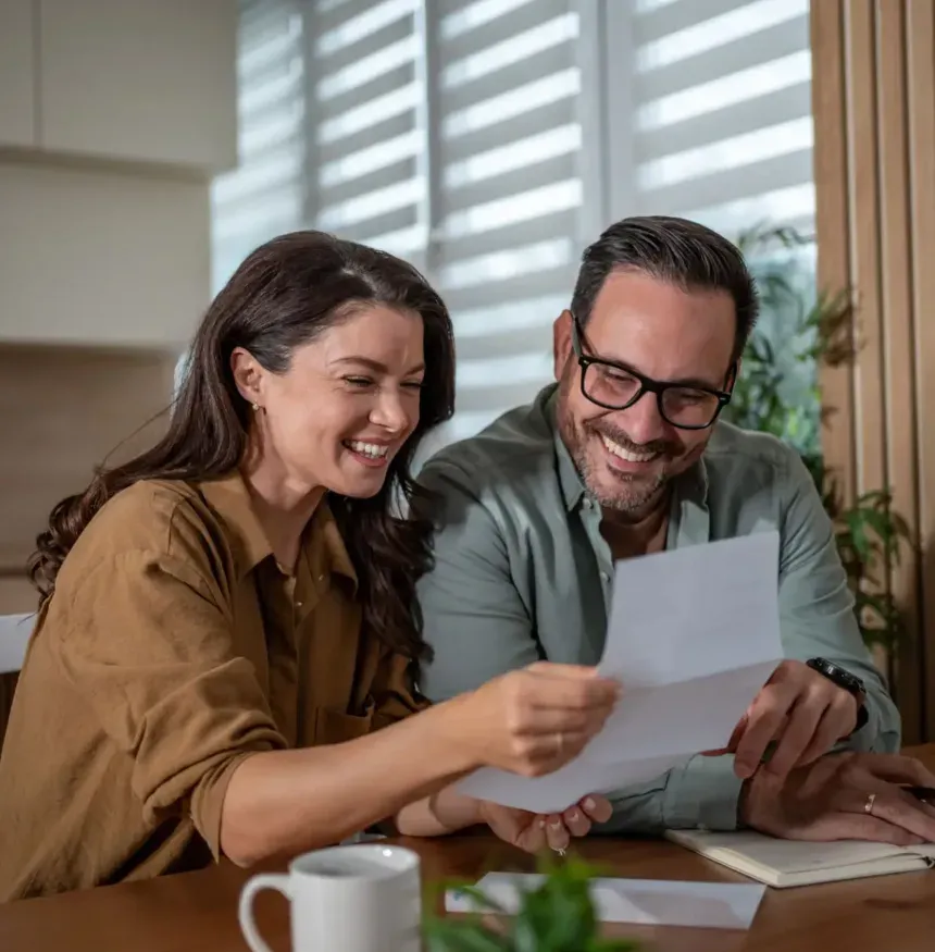 A couple laughing together over paperwork at their kitchen table