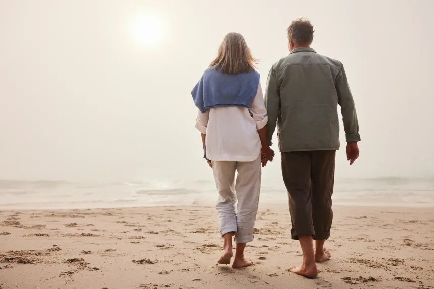 A retired couple walking the beach together, hand in hand, at sunrise