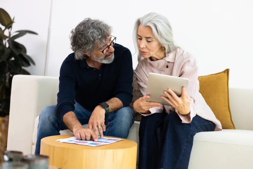 Mature couple discussing finances using a digital tablet and paperwork