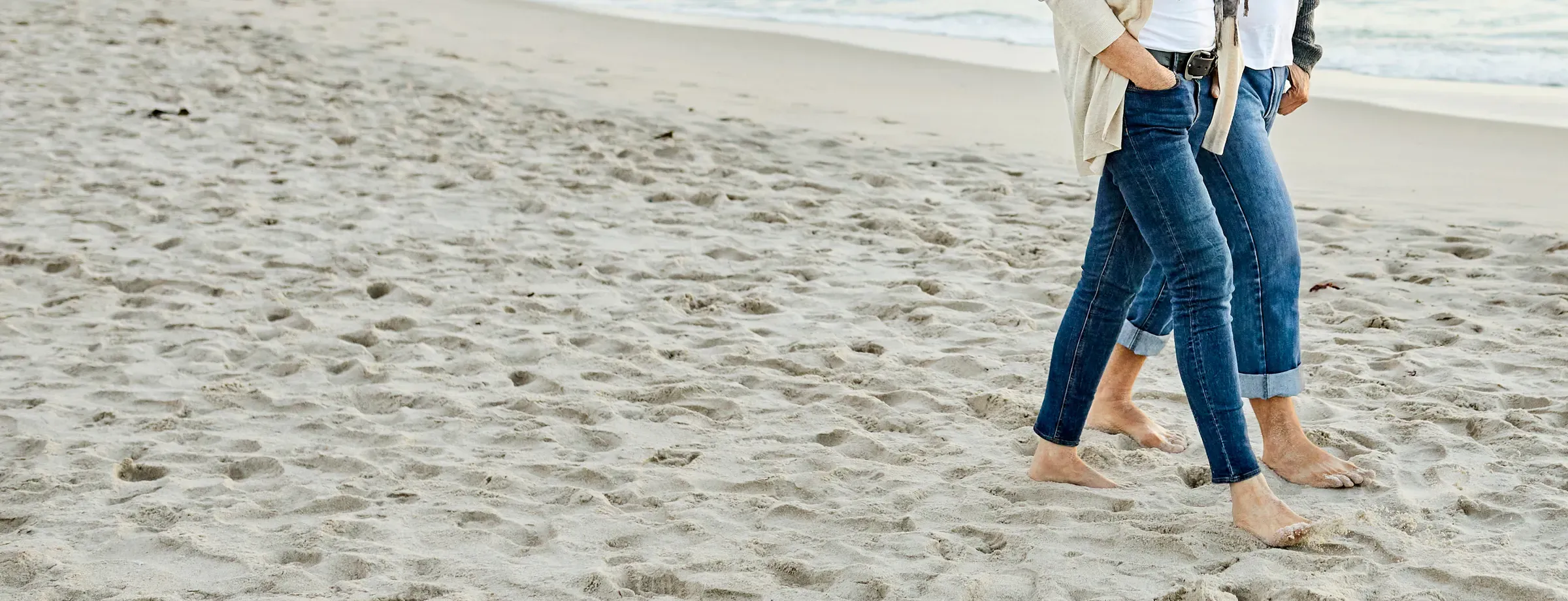 A couple walking barefoot along the sand, seen from the waist down