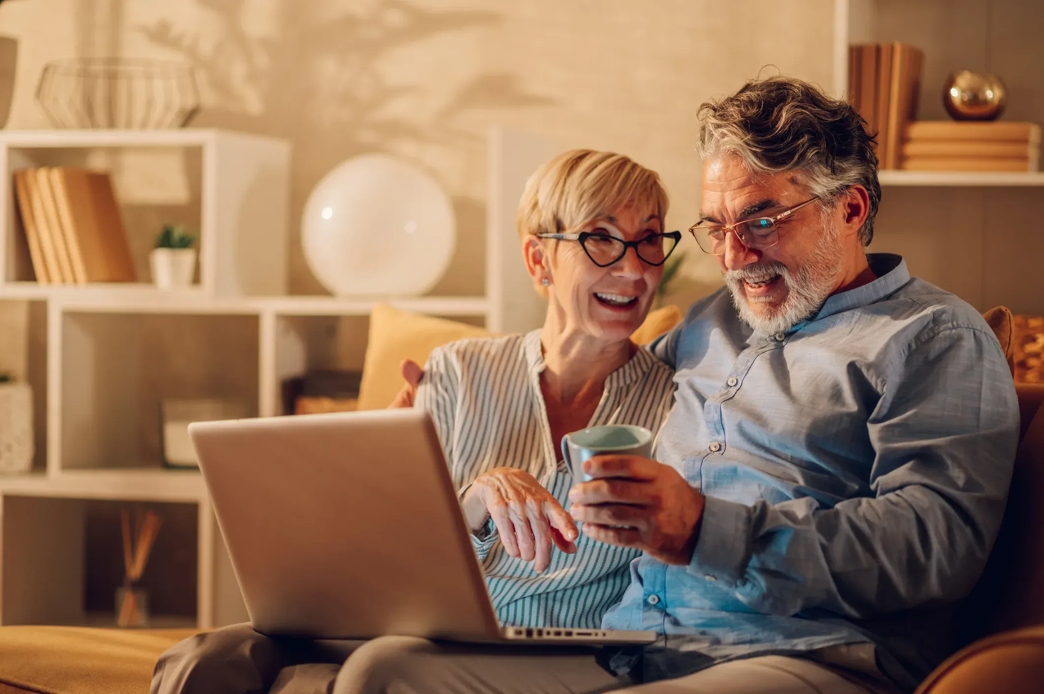 A couple on the sofa at home, laughing at something on the laptop between them